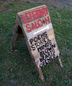 A wooden sign with hand-painted letters: Literary Salo+n, [arrow]. Poems, stories, minds blown, hearts opened